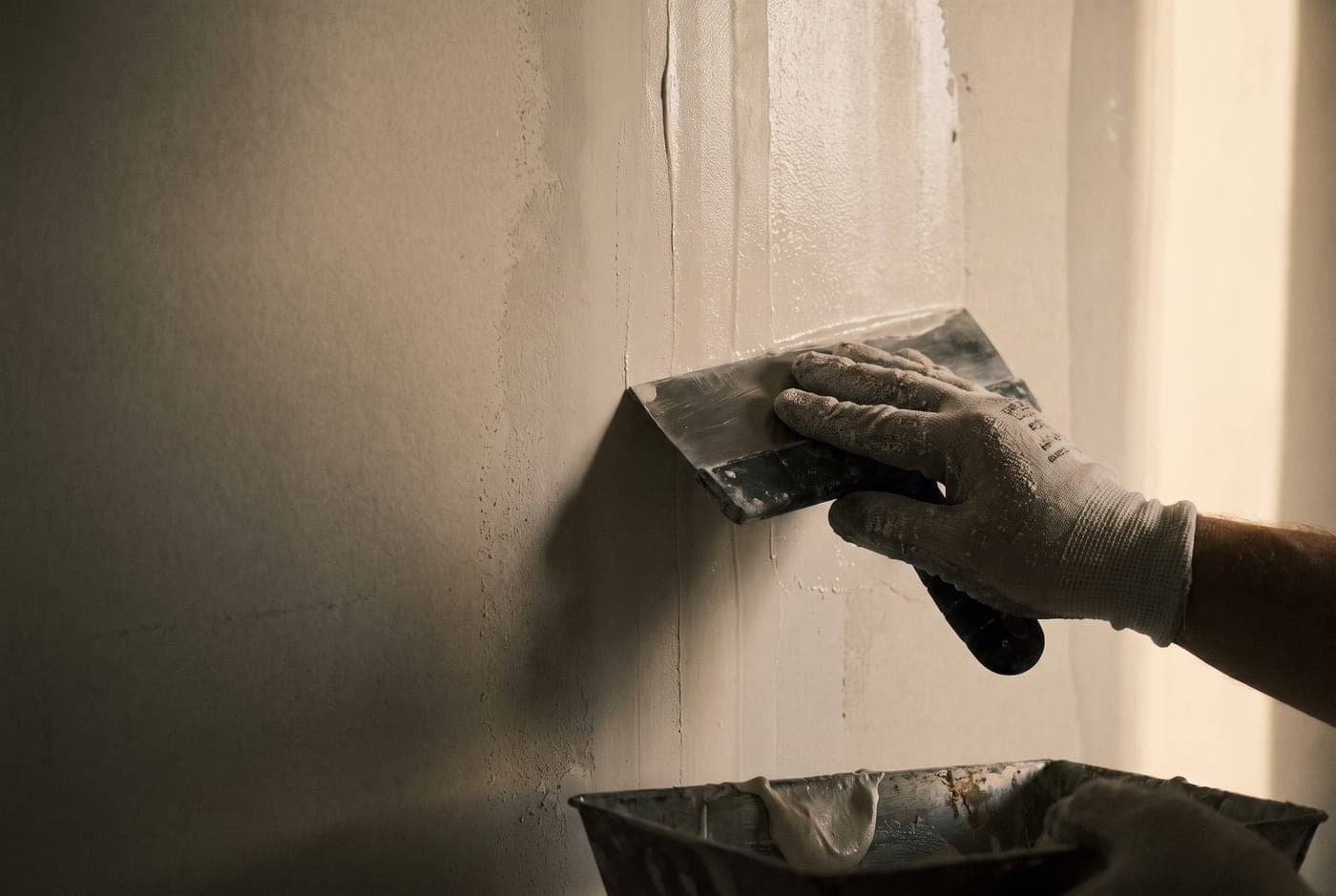 A finisher feathering joint compound over a taped seam with a wide taping knife